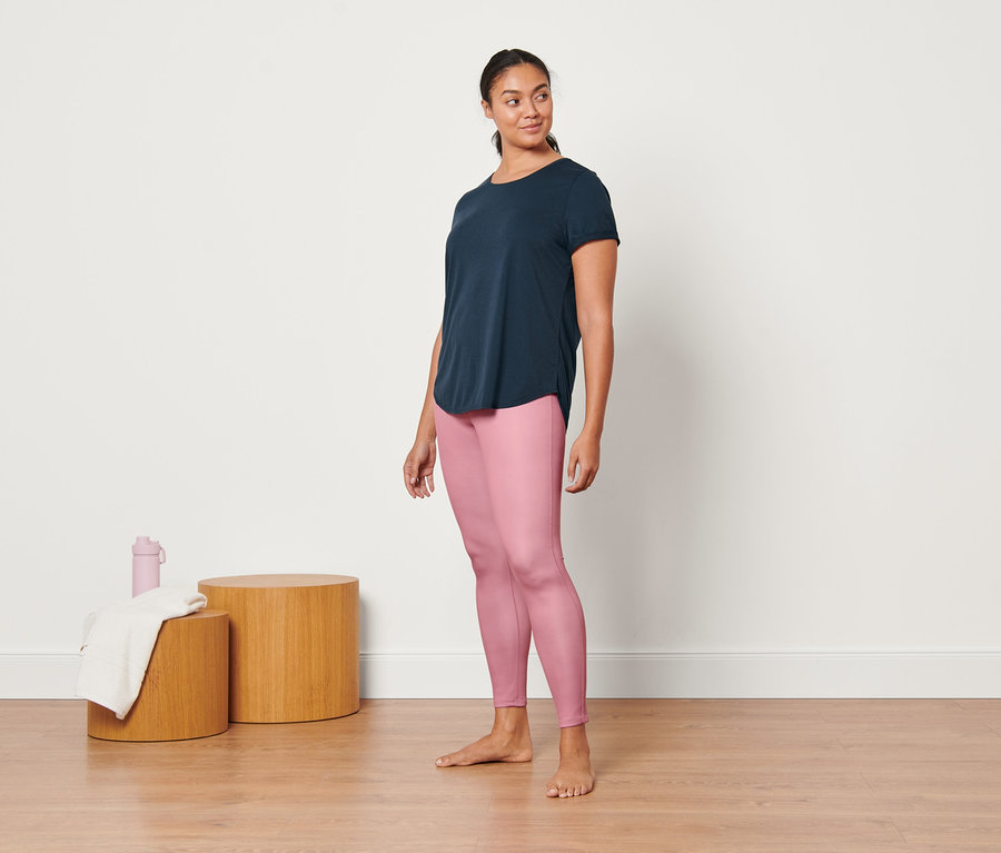 Une femme debout portant un legging de sport réversible rose et un t-shirt long bleu foncé.