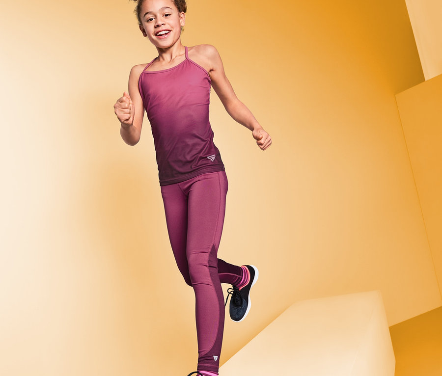 Une fille souriante en legging de sport pose sur un fond jaune.