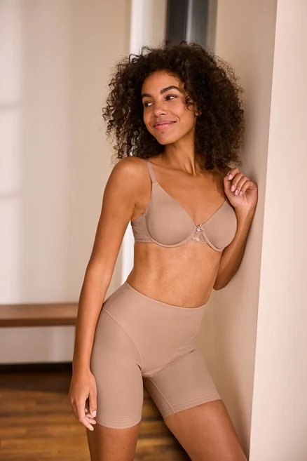 Une femme pose en short « Shaping » beige et soutien-gorge à armatures beige.