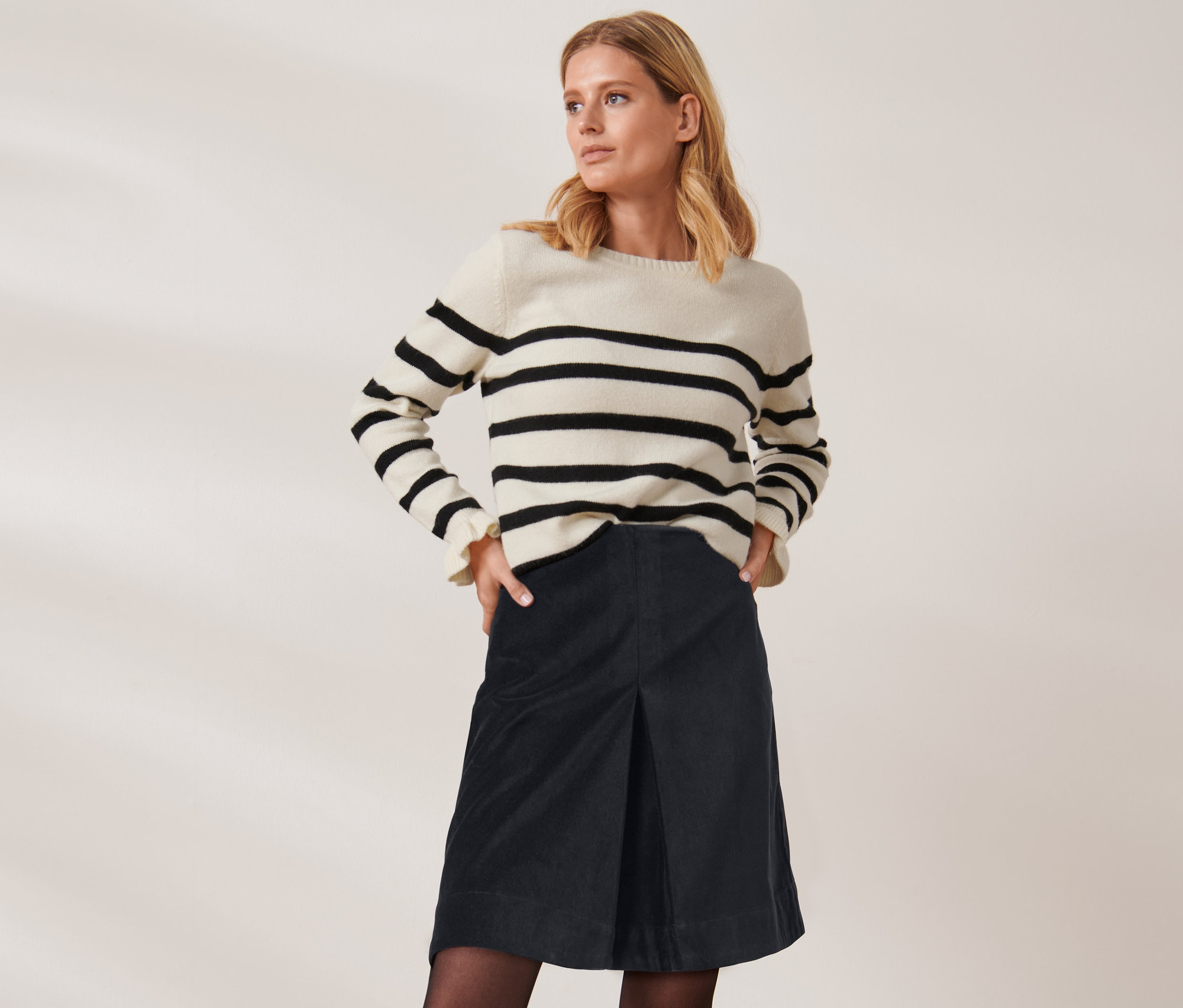 Femme blonde posant en pull rayé et jupe courte en velours.