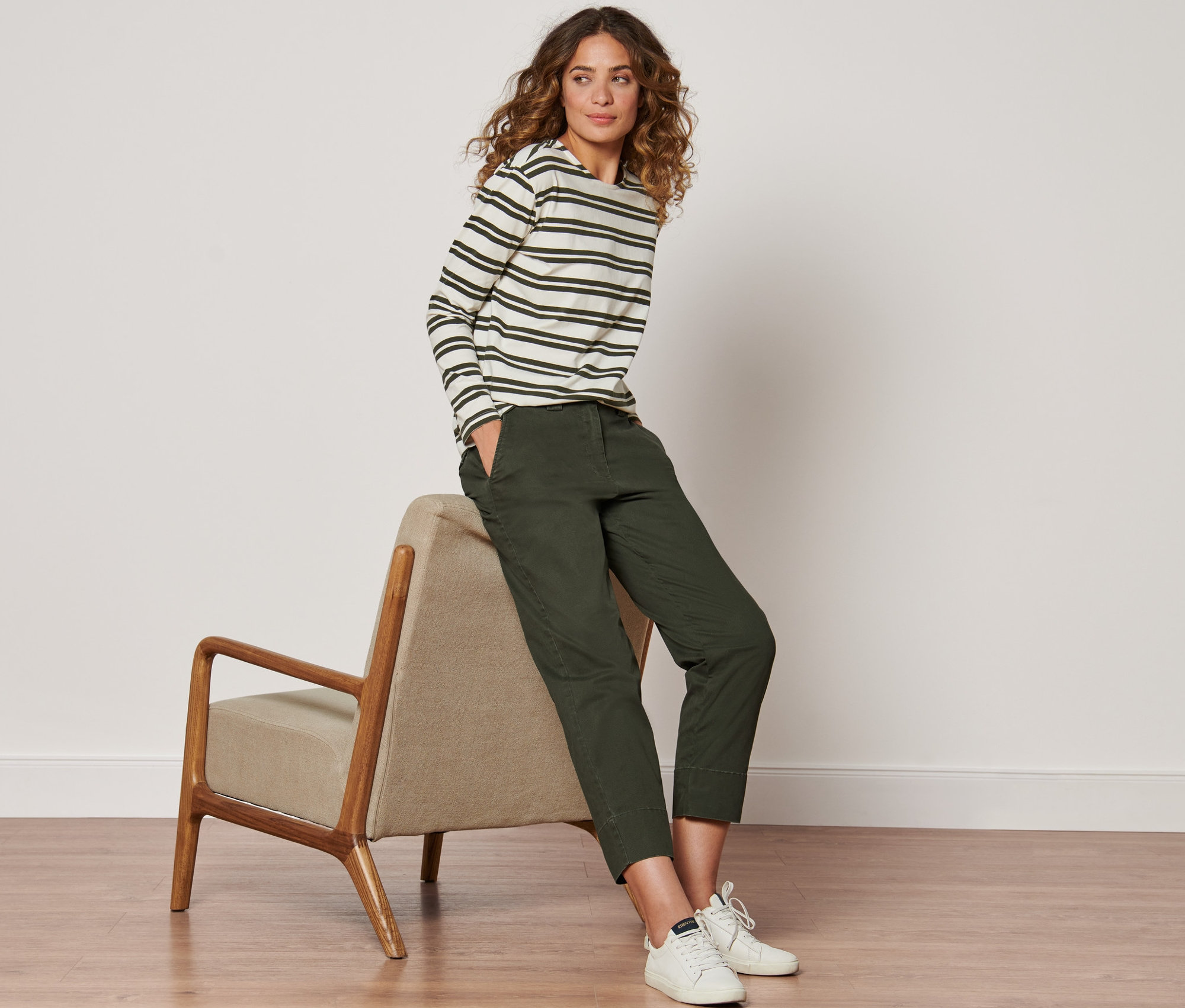 Femme assise sur une chaise portant un pantalon chino olive et un t-shirt rayé.