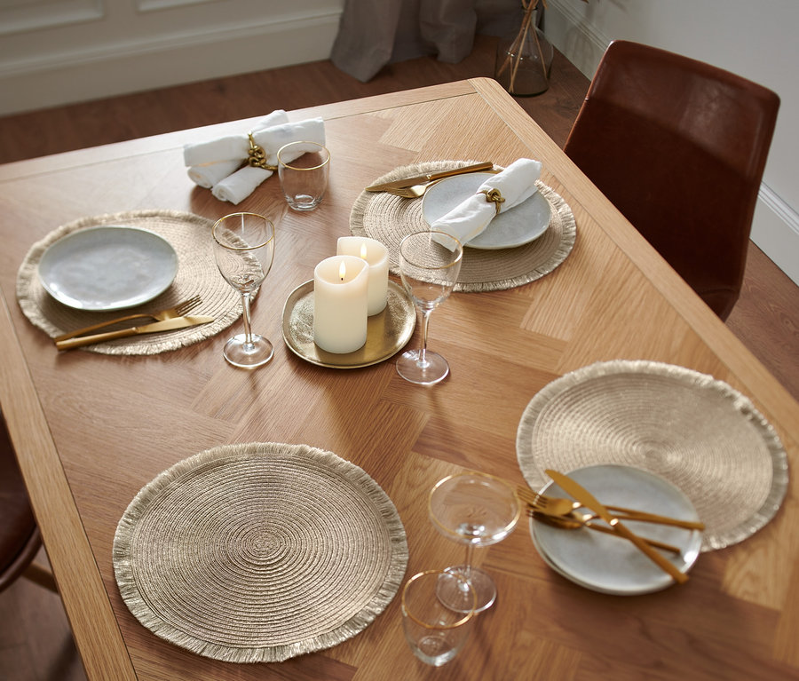 Sur une table en bois, il y a quatre sets de table de couleur or.