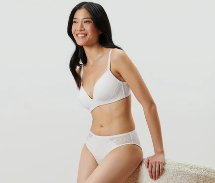 Une femme est assise et porte un soutien-gorge blanc et 2 slips, blanc.