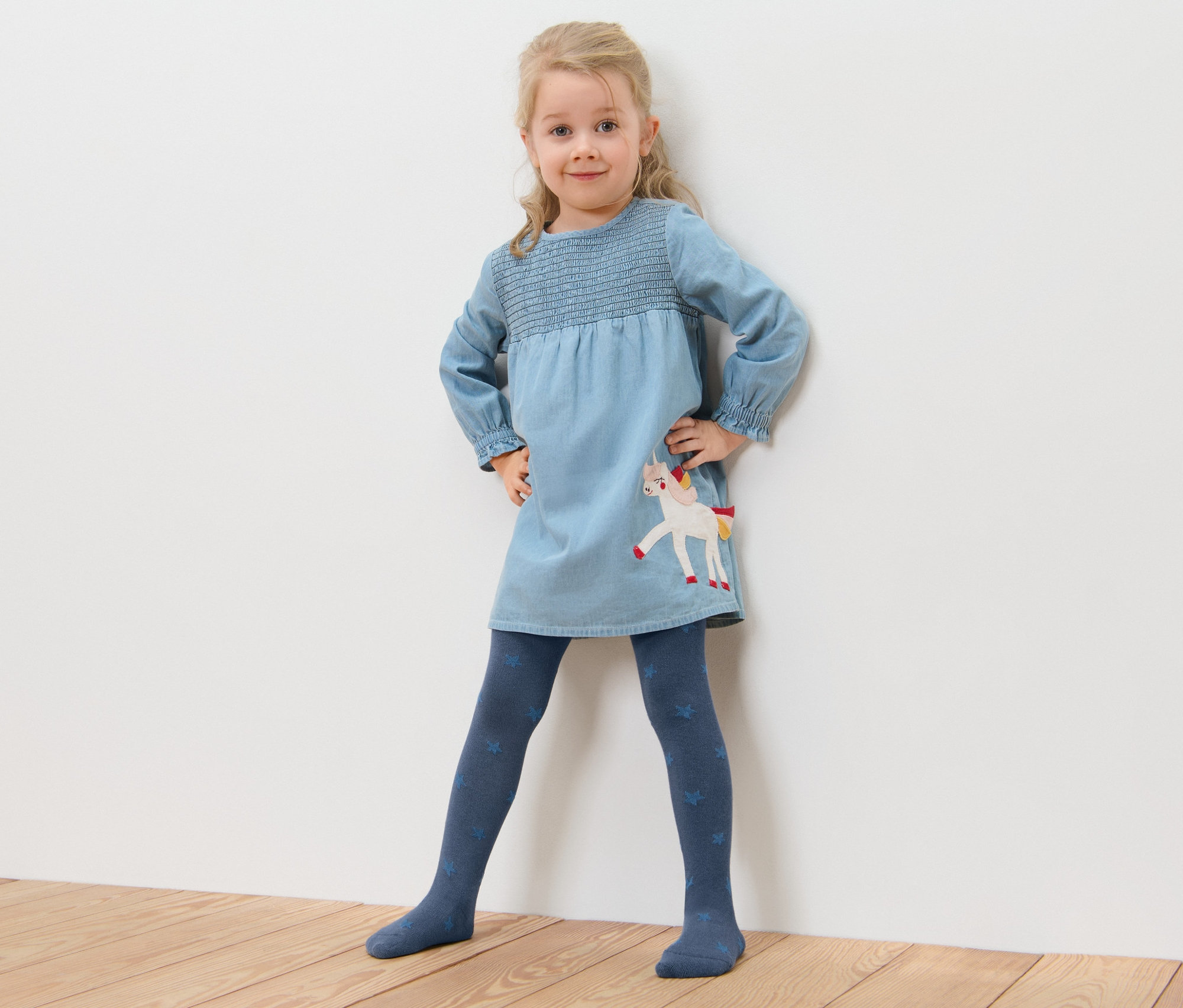 Fillette posant dans une robe bleue avec une licorne et 5 collants en coton étoilés.