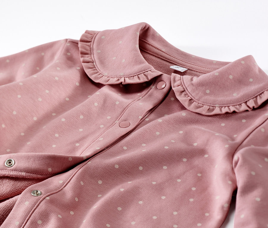 Détail d'une veste en sweat rose avec volant pour enfant et pois blancs.