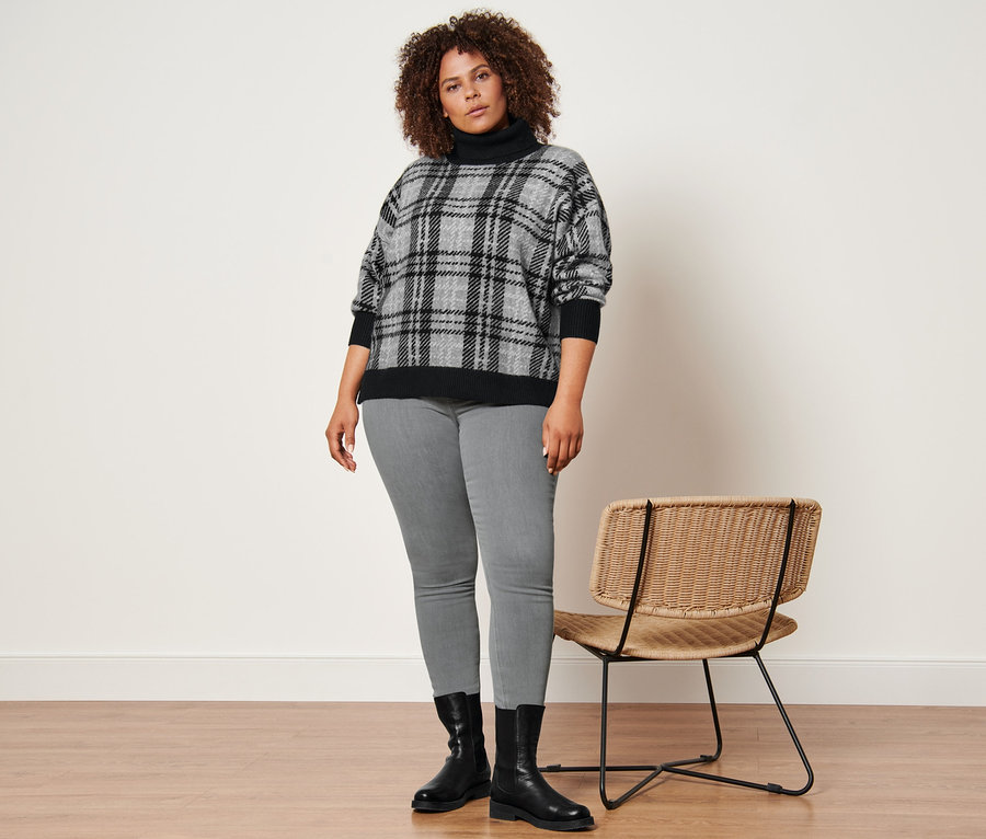 Femme posant portant un pull en maille à col roulé, un tregging gris chiné et des bottines en cuir.