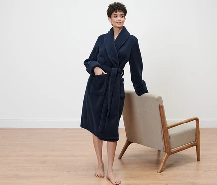 Femme debout en robe de chambre, appuyée sur un fauteuil.