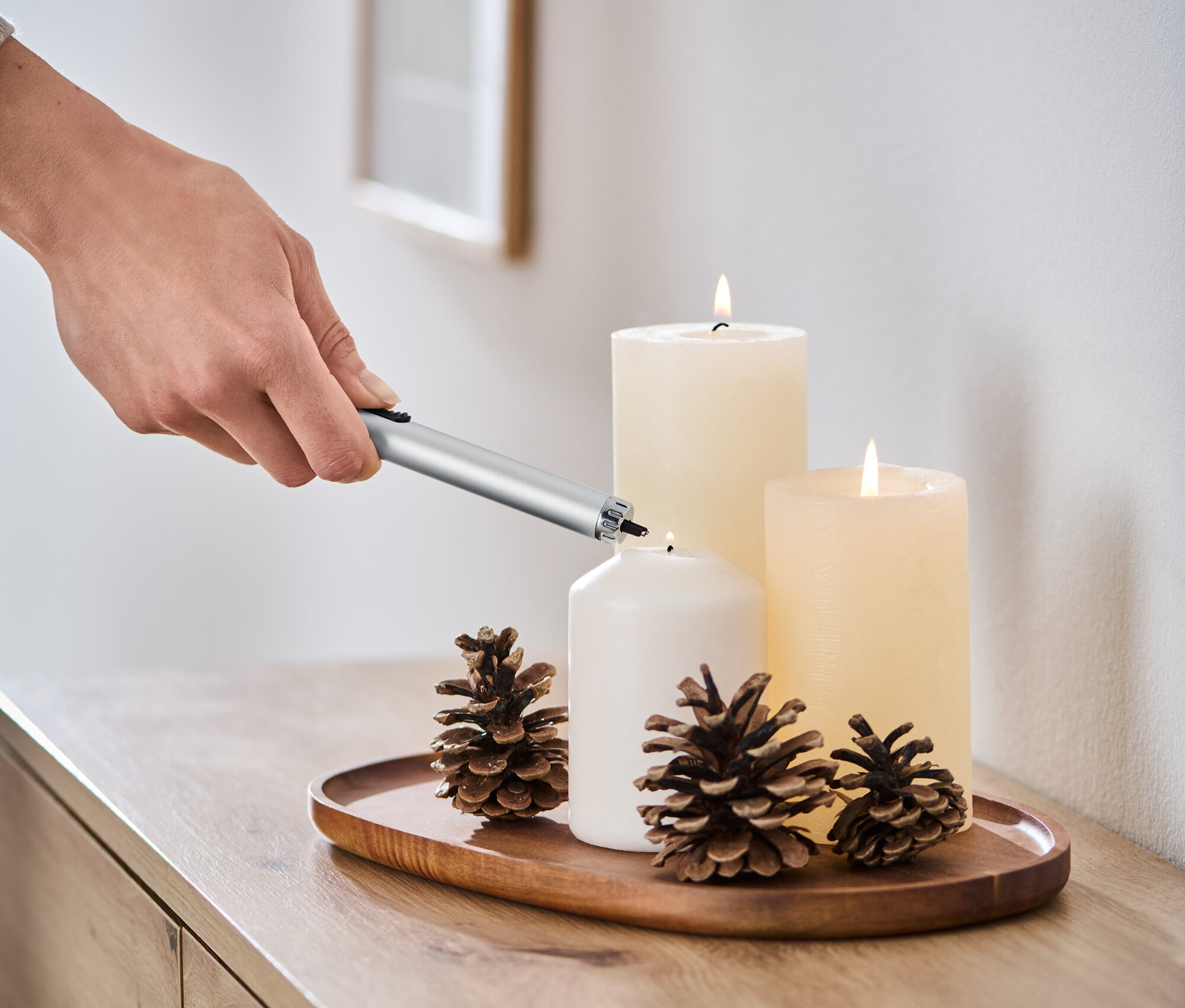 Une main allume une bougie blanche avec un allume-gaz électrique à arc lumineux.