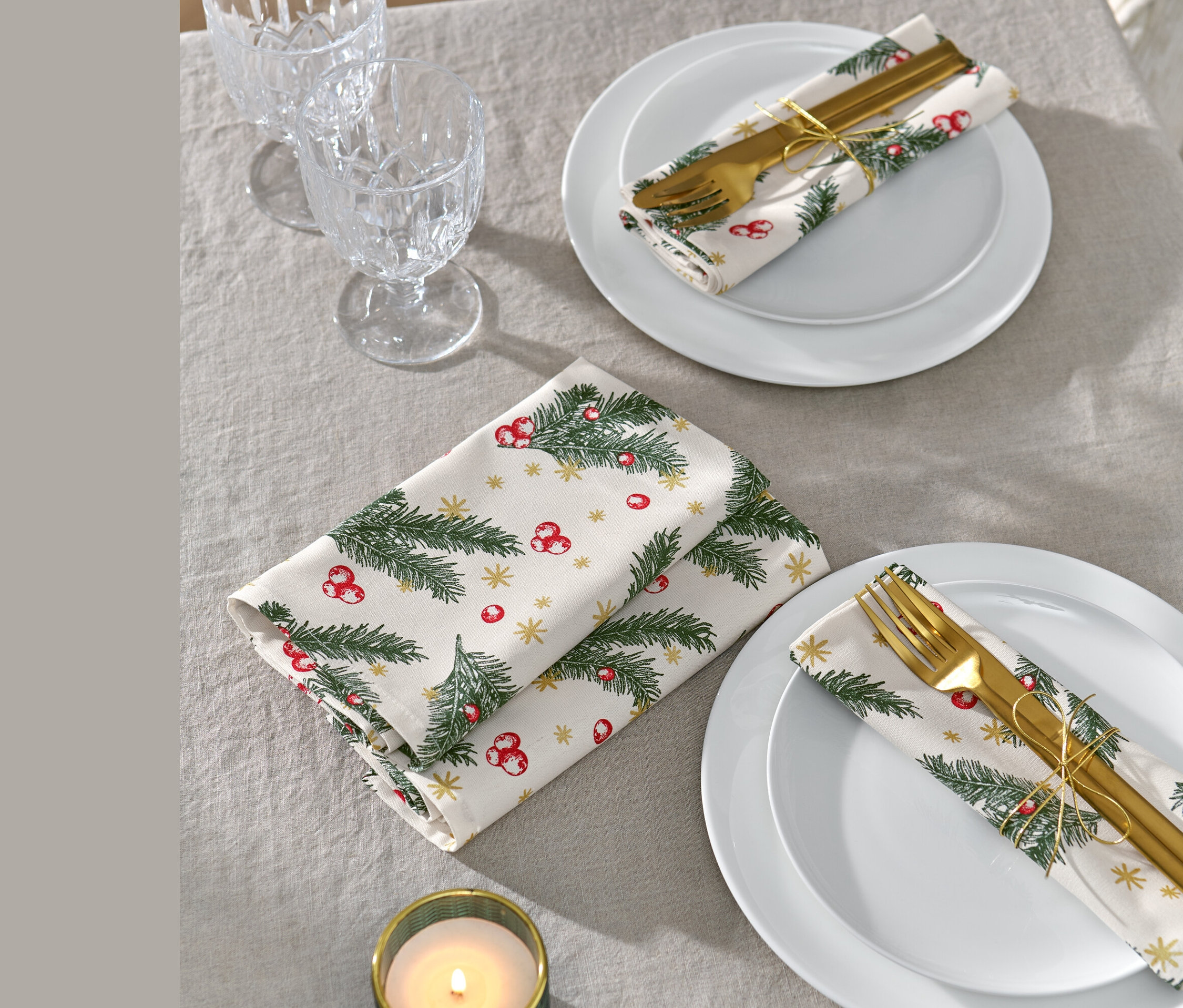 Deux assiettes blanches avec 4
serviettes de Noël, des couverts et des verres sur une nappe grise.