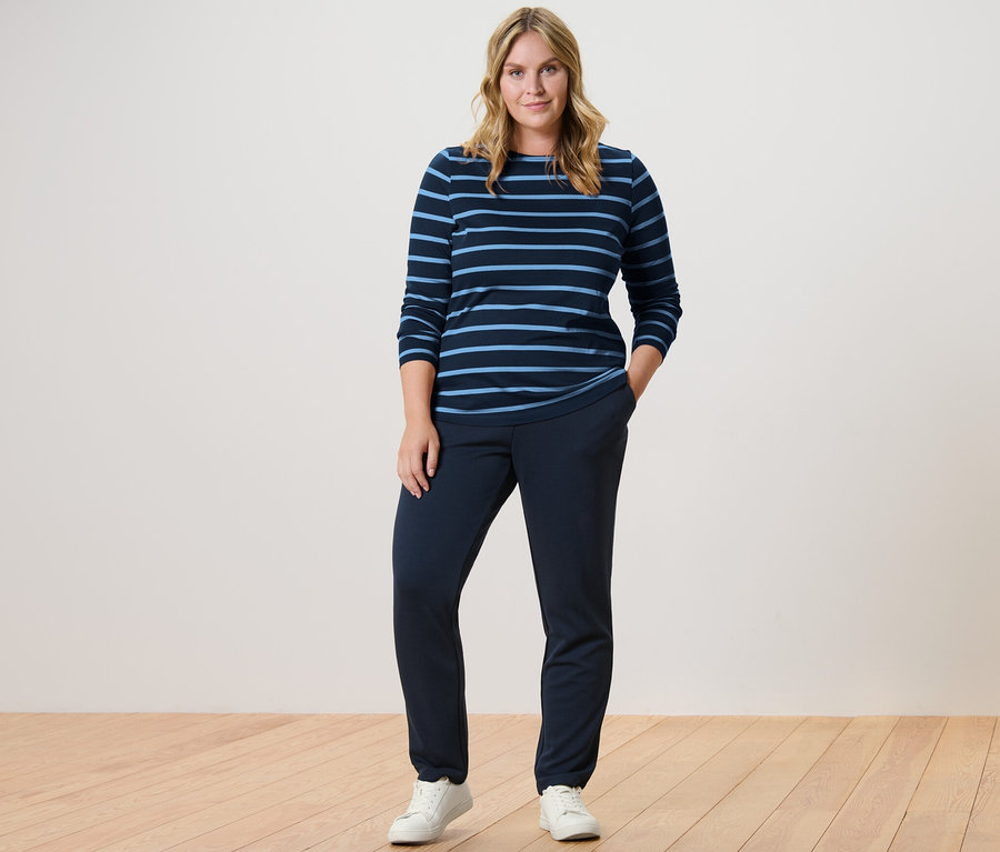 Une femme debout portant un pantalon de jogging bleu marine et un t-shirt rayé à manches longues.