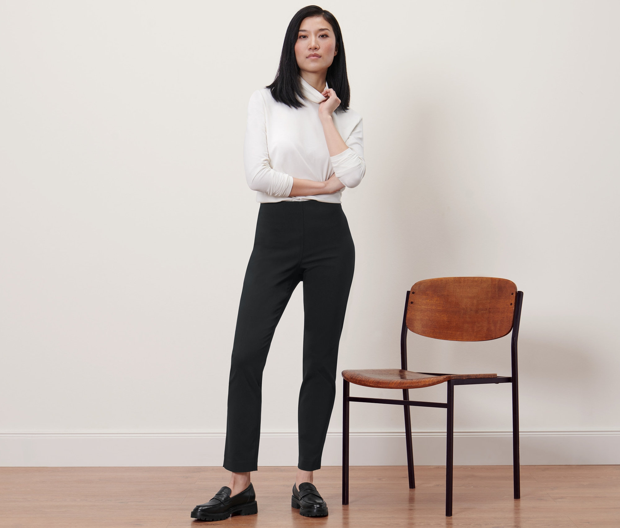 Femme posant en pantalon stretch noir à côté d'une chaise.