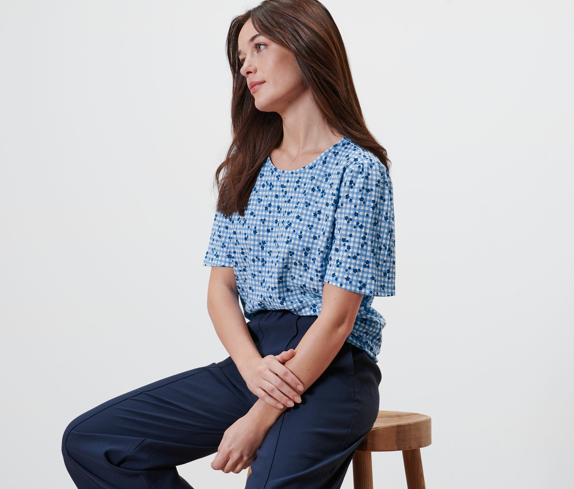Femme assise sur un tabouret portant une blouse bleue avec imprimé intégral.