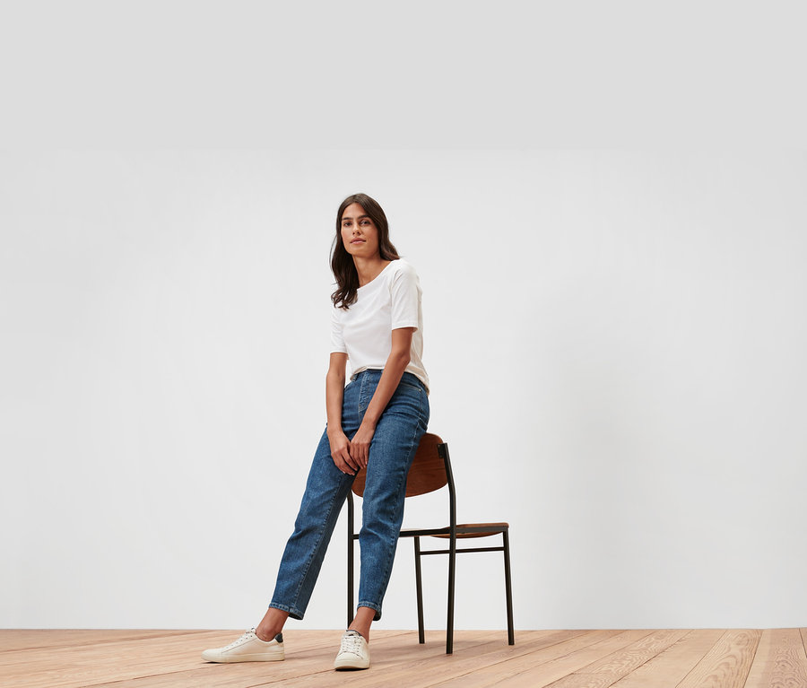 Une femme est assise sur une chaise et porte un jean mom – Coupe « Nyla » et un t-shirt blanc.