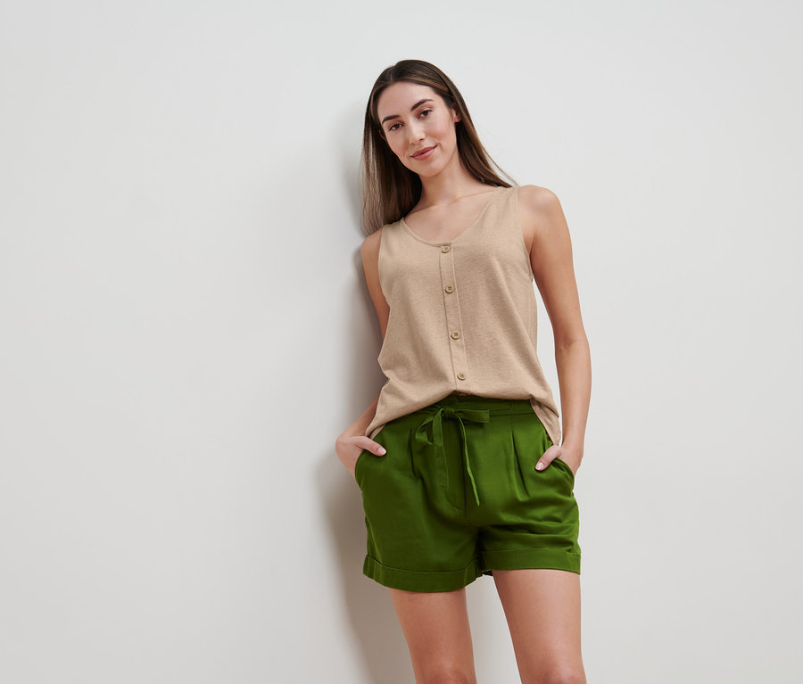 Femme posant en haut beige chiné avec patte de boutonnage et short vert.