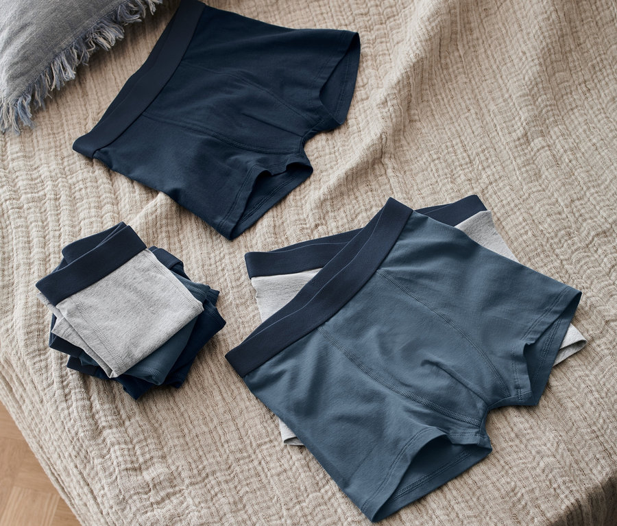 Sur un lit se trouvent 7 boxers pour enfant bleus et gris.
