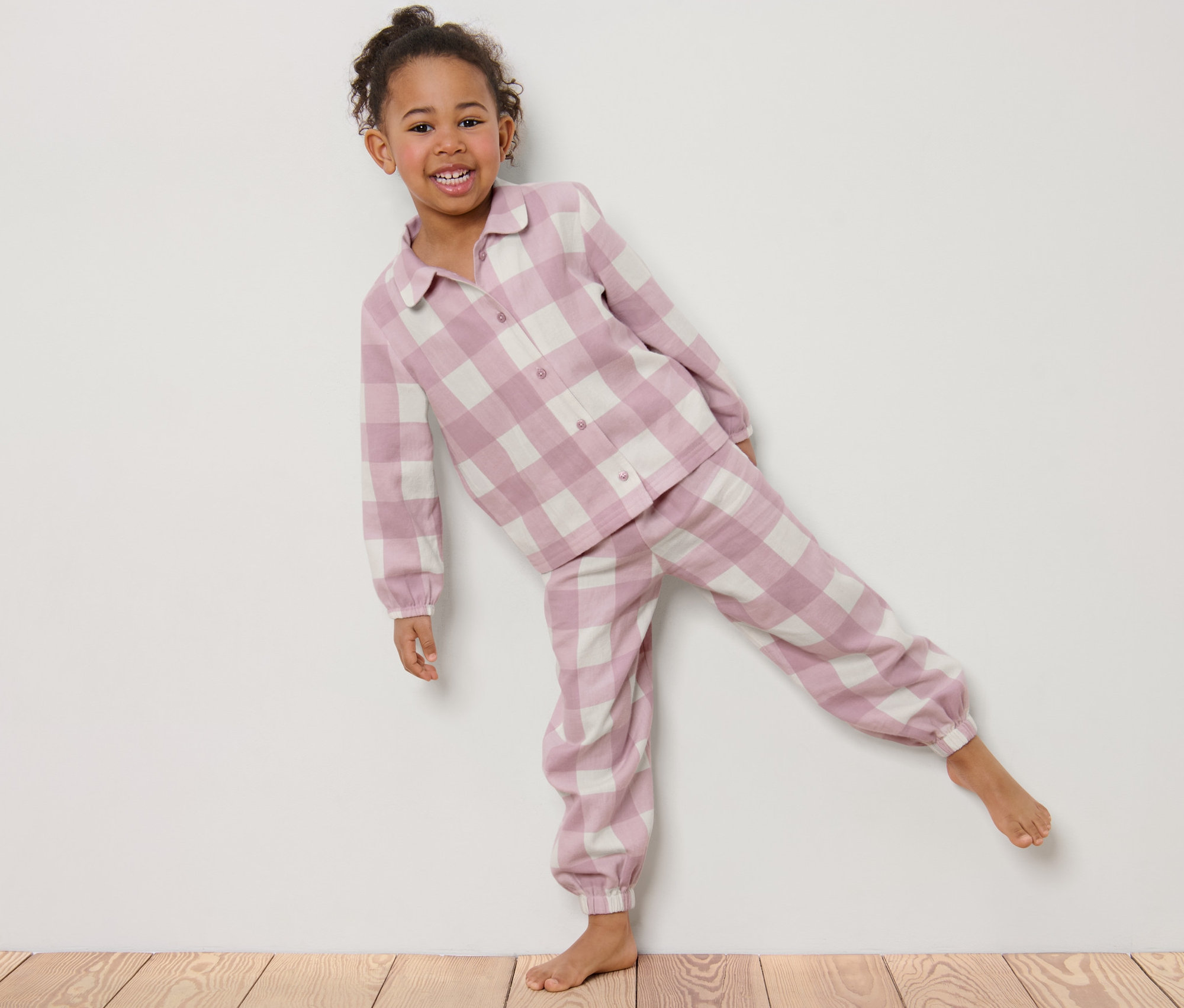 Une fillette souriante pose en pyjama en flanelle à carreaux.