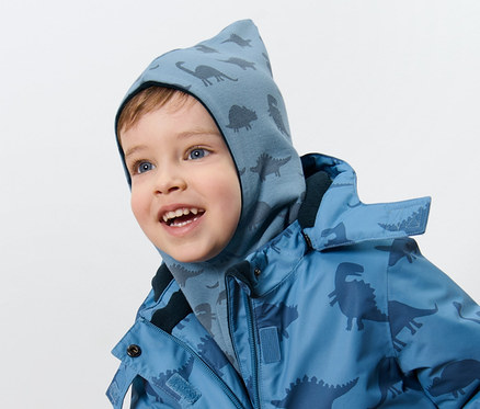 Un garçon porte une cagoule réversible pour enfant, dinosaure et une veste à motif dinosaure.