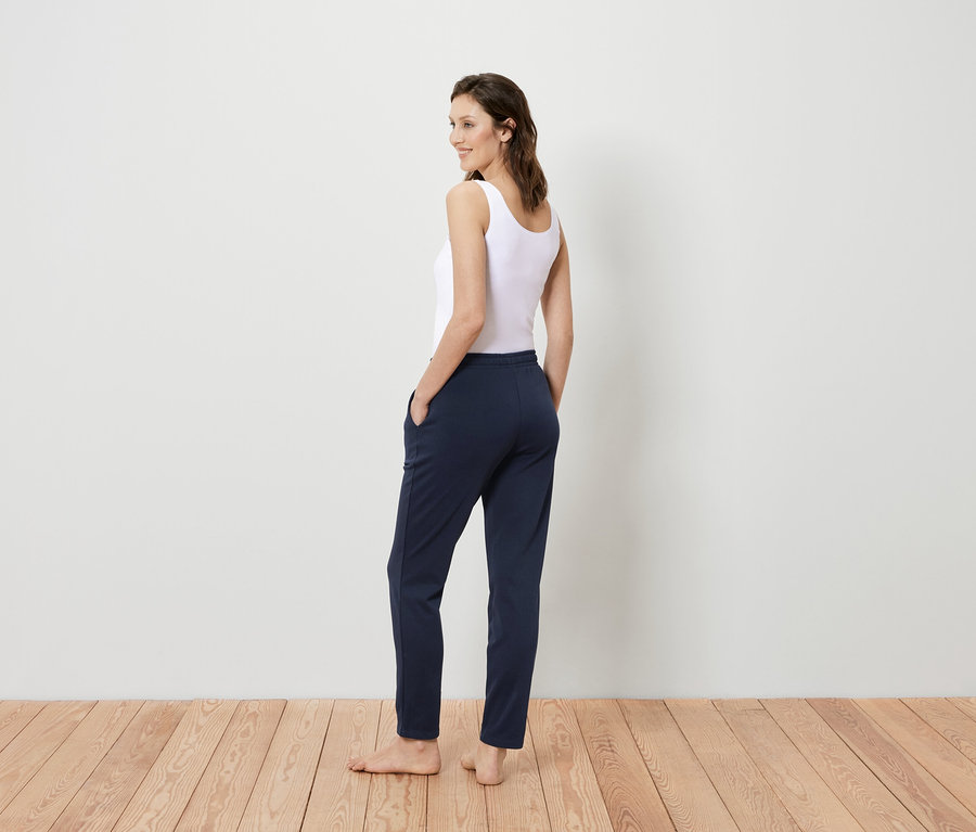Une femme en débardeur blanc et pantalon bleu marine se tient dos à la caméra et regarde par-dessus son épaule.