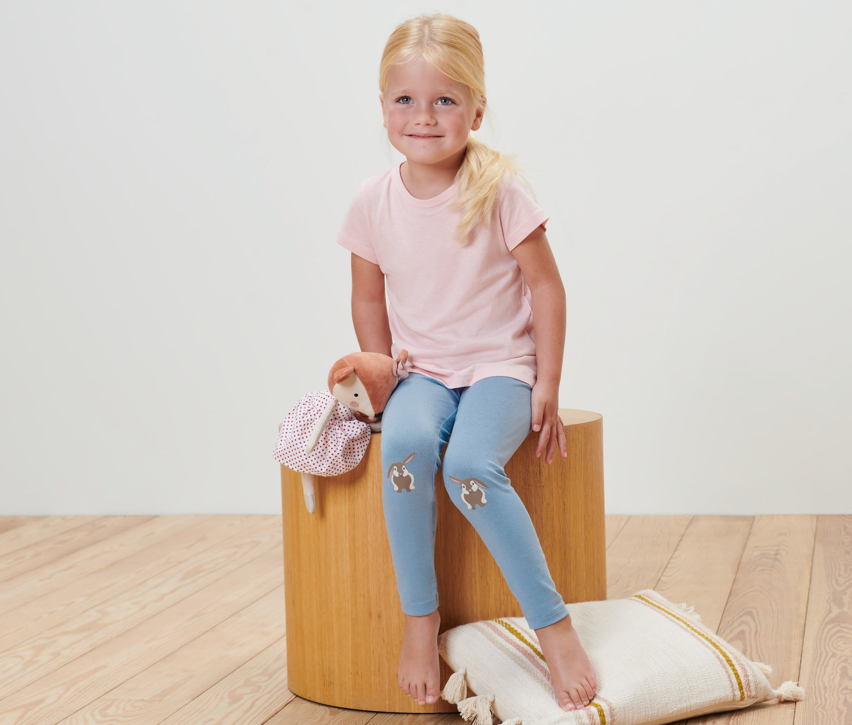 Une fille est assise sur un tabouret et porte 2 leggings pour bébé rayés.