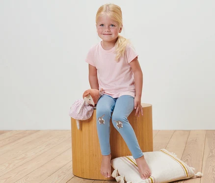 Une fille est assise sur un tabouret et porte 2 leggings pour bébé rayés.