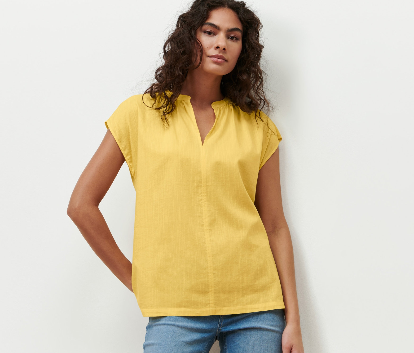 Femme posant en chemisier jaune à manches courtes et jean bleu.