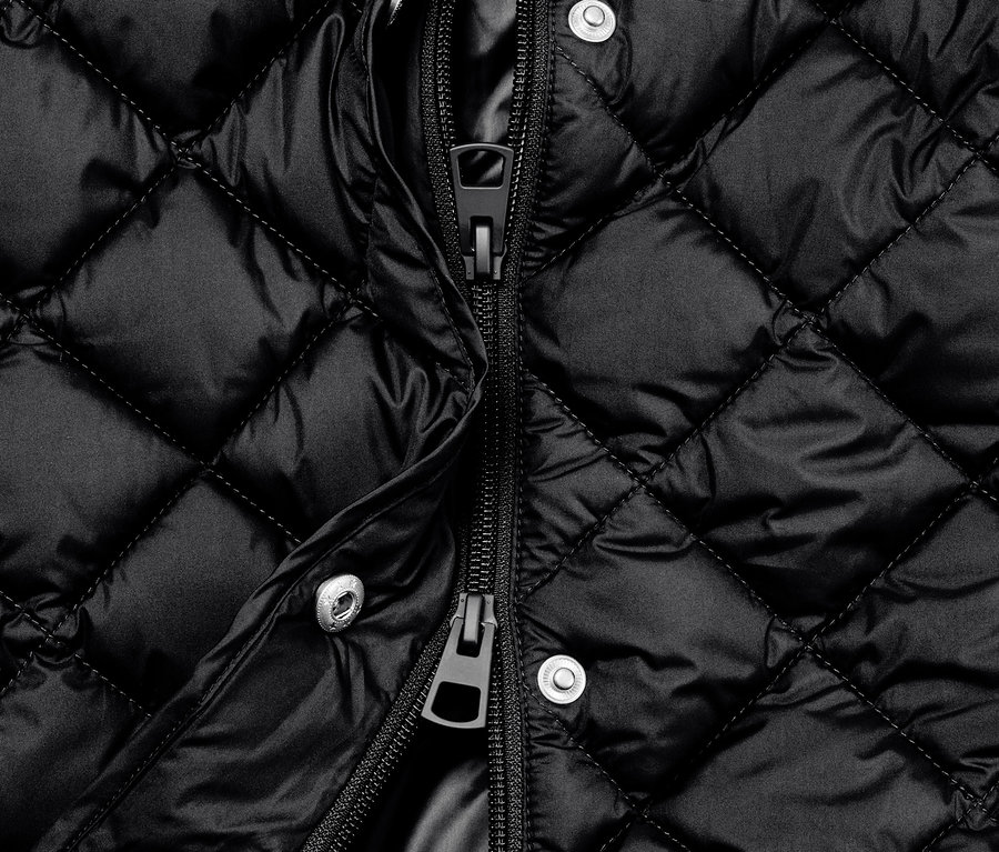 Gros plan sur un long gilet noir matelassé avec capuche et fermeture éclair ouverte.