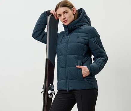 Femme posant en veste de ski matelassée bleu marine, appuyée sur des skis.