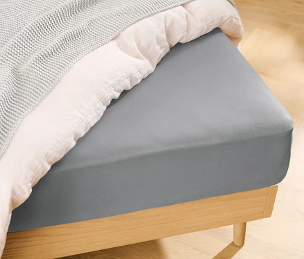 Vue détaillée d'un lit avec un drap-housse en jersey gris.
