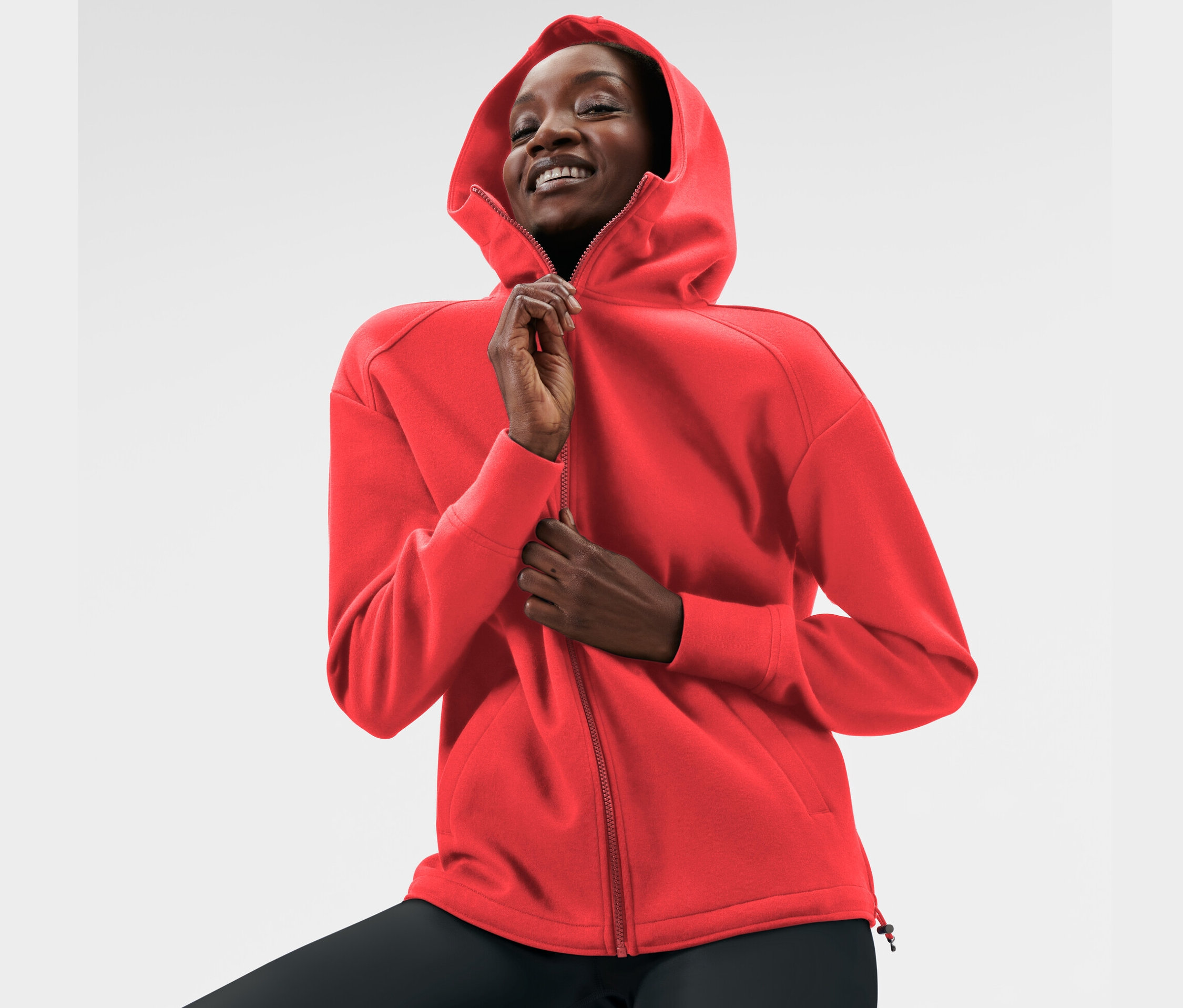 Femme fermant une veste à capuche en sweat rouge.