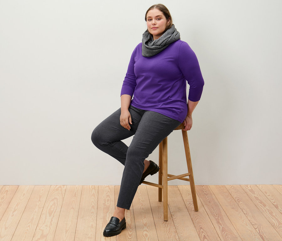 Femme assise sur un tabouret portant un pantalon stretch et un t-shirt violet à manches 3/4.