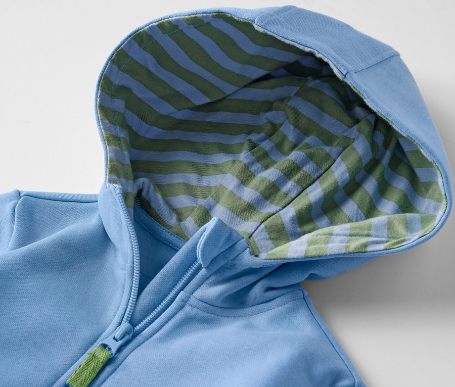 Gros plan sur un sweat à capuche bleu clair pour enfant avec un intérieur rayé bleu et vert et une fermeture éclair.