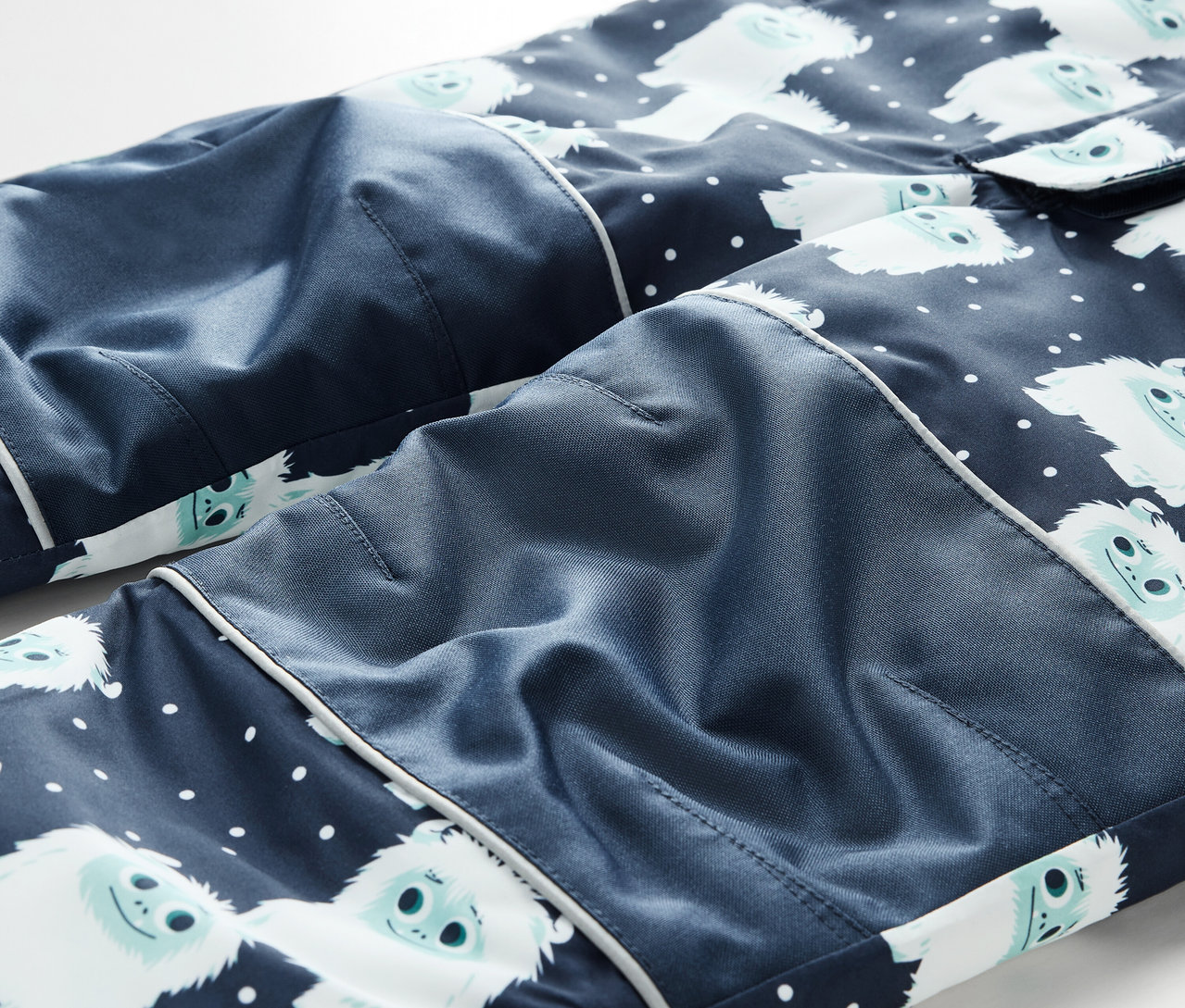 Détail d'un pantalon de pyjama bleu marine avec des bonhommes de neige blancs et des pois blancs.