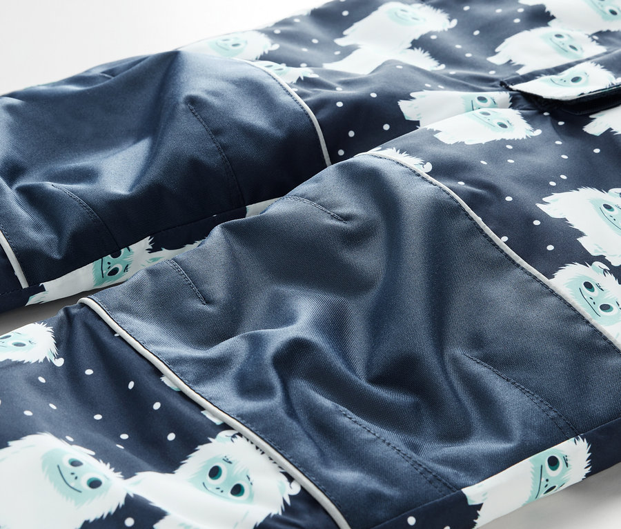Détail d'un pantalon de pyjama bleu marine avec des bonhommes de neige blancs et des pois blancs.
