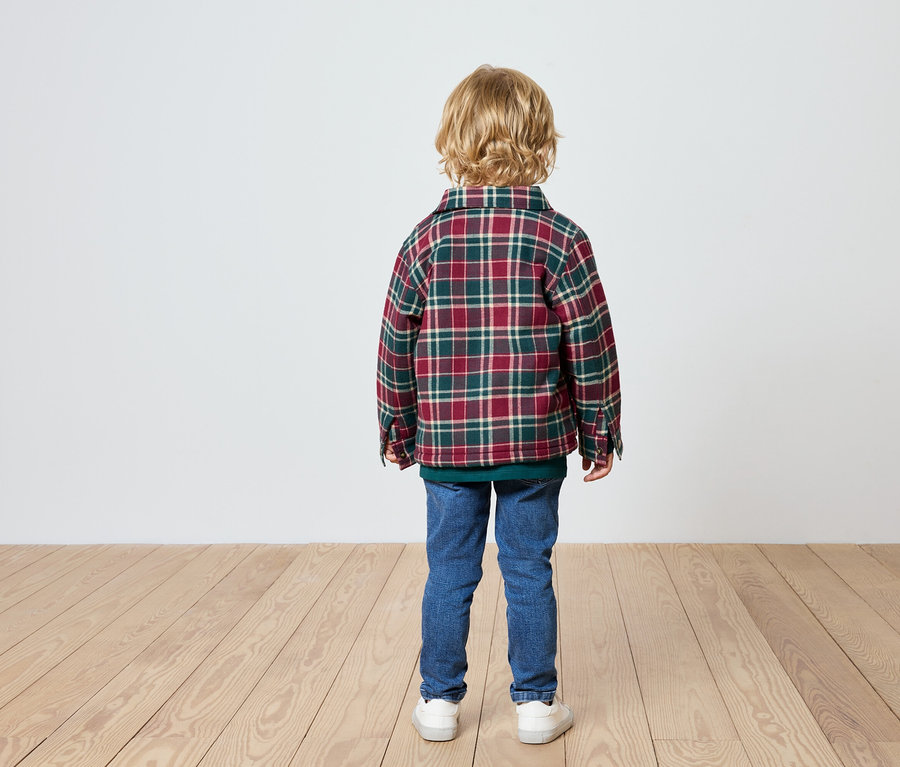 Garçon debout, dos à la caméra, portant une chemise à carreaux, un jean et des baskets.
