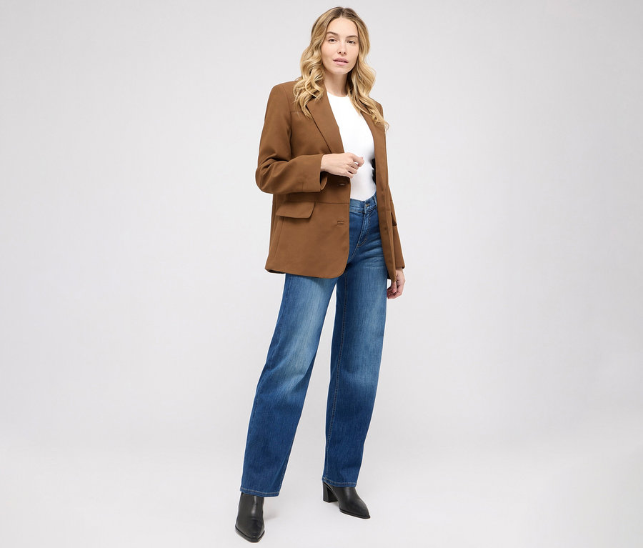 Femme posant en jean Angels « Liz » jambes larges, bleu moyen usé, un t-shirt blanc et un blazer marron.