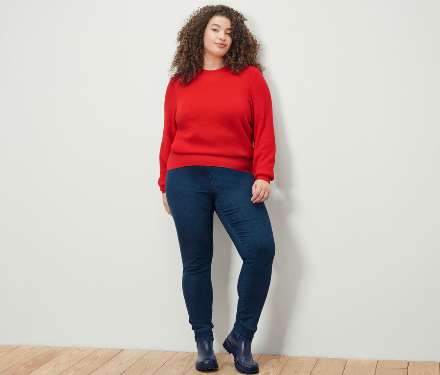 Femme posant en pull en maille fine rouge et legging taille haute en denim.