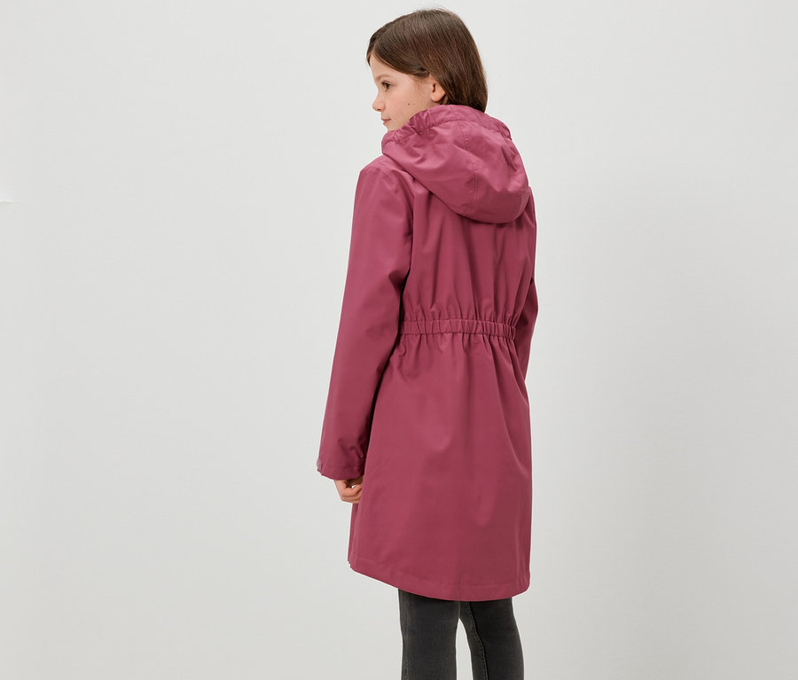 Une fille se tient dos à la caméra et porte une parka de pluie pour enfants.