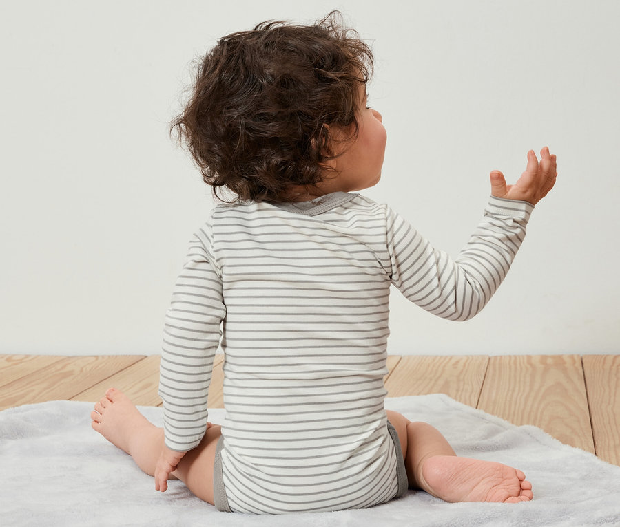Un bébé est assis dos à la caméra sur un tapis et porte un ensemble de 5 bodys évolutifs.