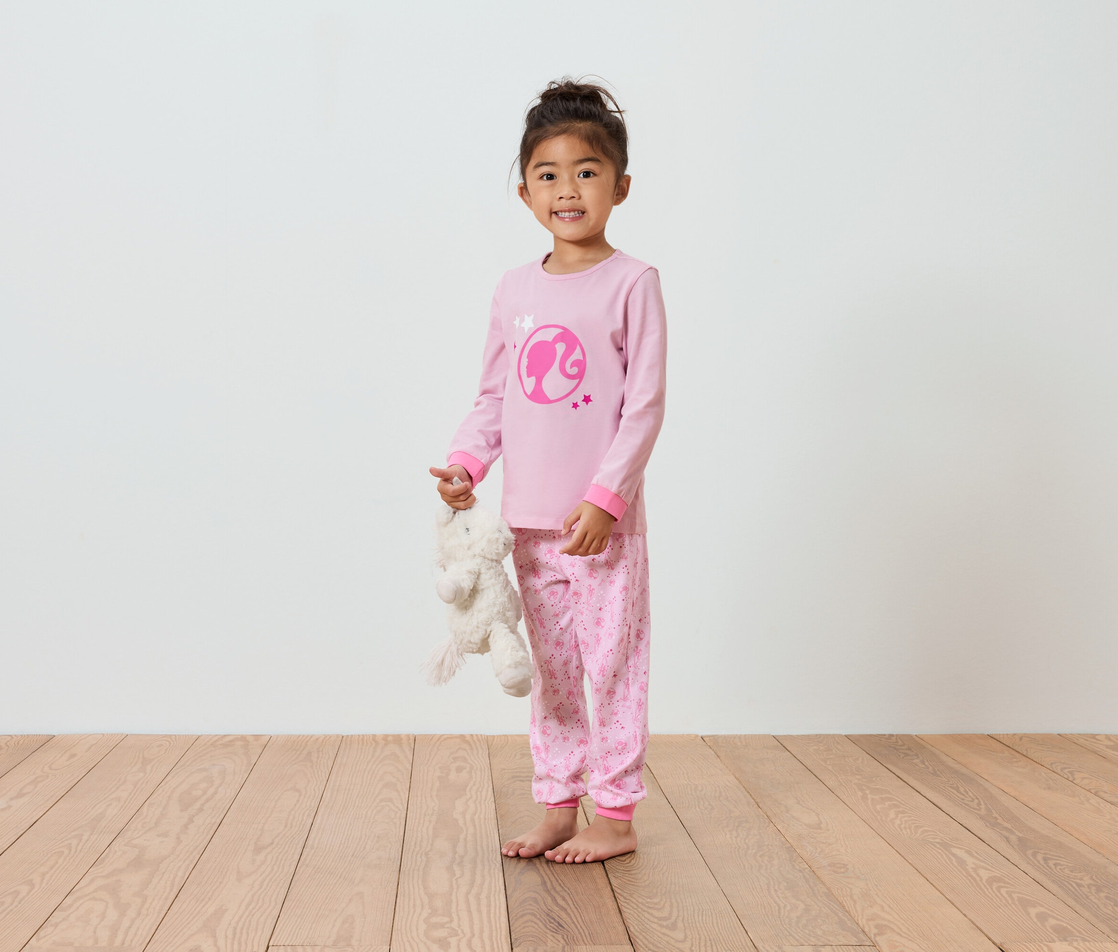 Une fille en pyjama rose Barbie tenant un ours en peluche.