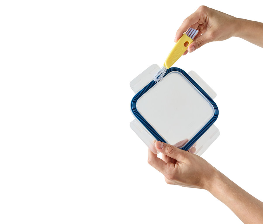 Des mains nettoient le bord d'un récipient transparent à cadre bleu avec une brosse jaune.