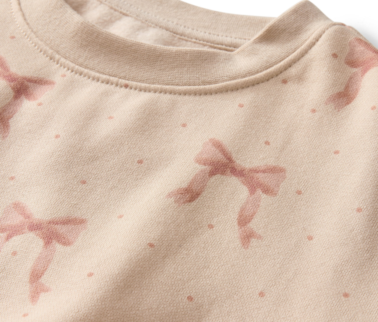 Gros plan sur un sweat-shirt beige avec un motif de nœuds roses et de points.