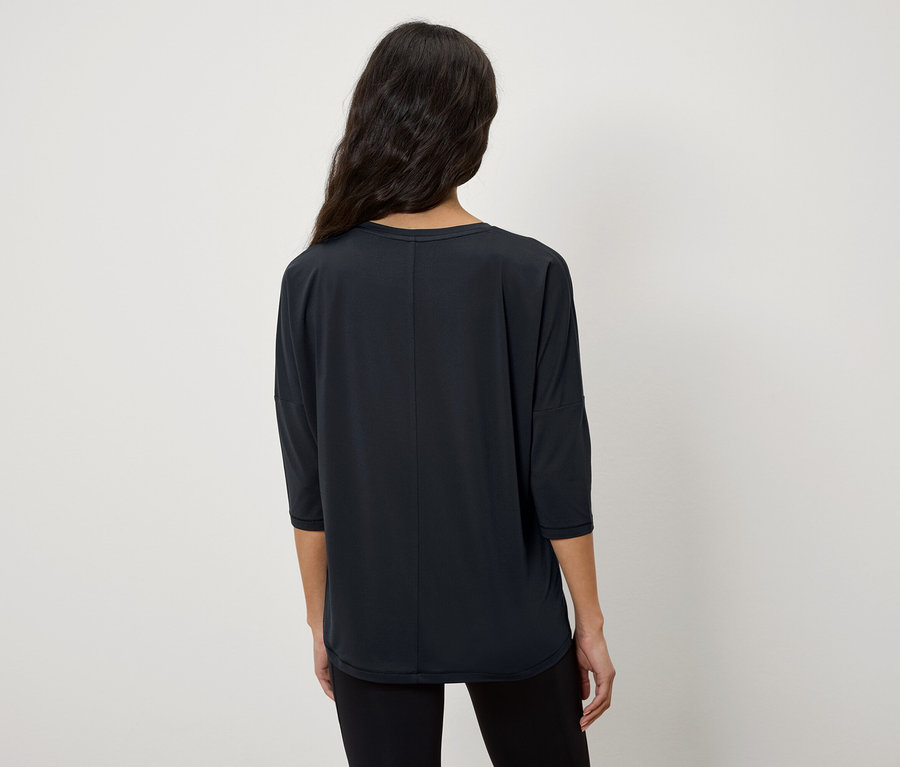Une femme, dos à la caméra, porte un t-shirt noir à manches trois-quarts.