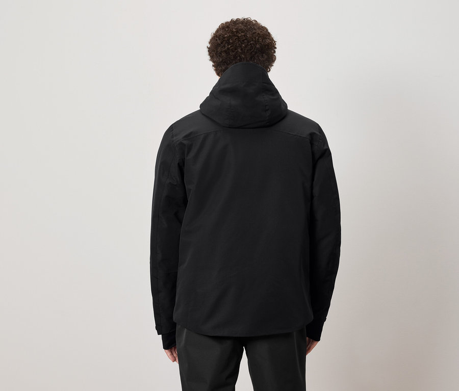 Un homme aux cheveux bouclés se tient dos à nous et porte une veste à capuche noire.