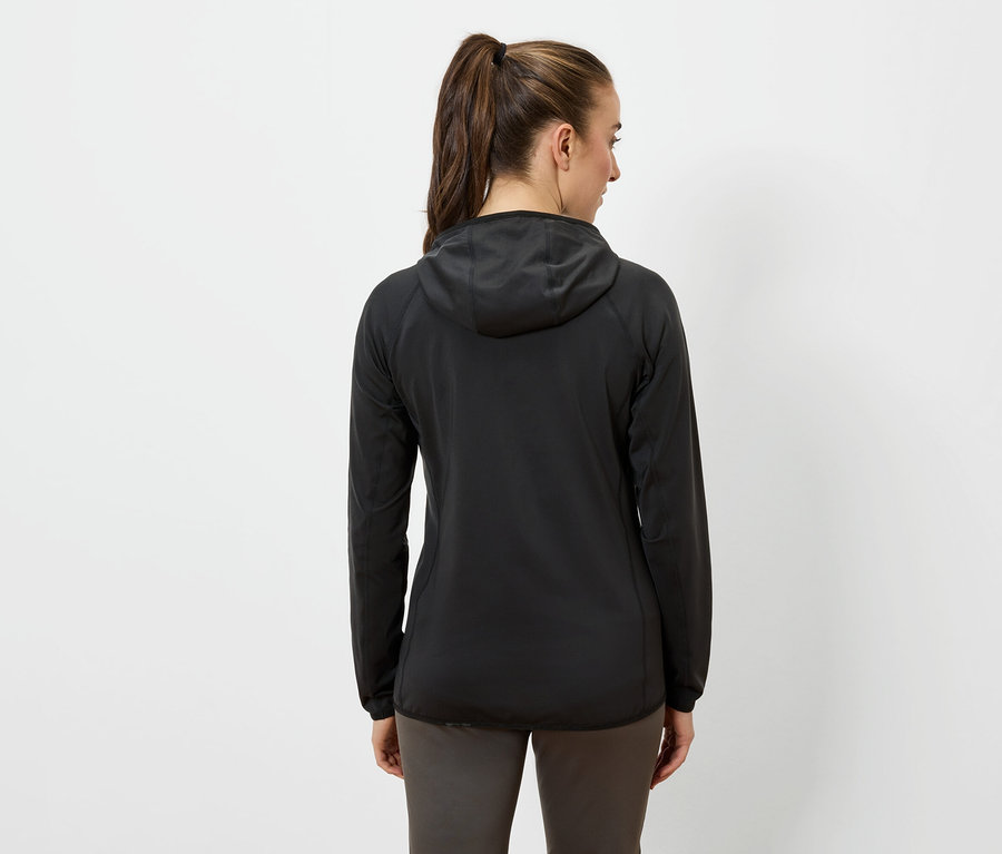 Une femme, vue de dos, porte une veste à capuche noire et un pantalon foncé.