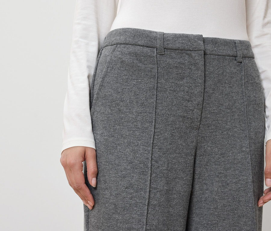 Une femme porte un pantalon gris et un haut blanc.