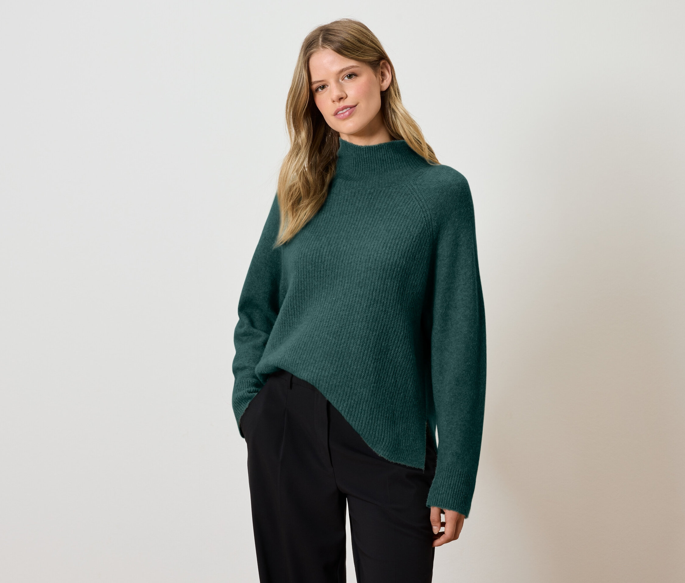 Femme posant en pull vert et pantalon noir.