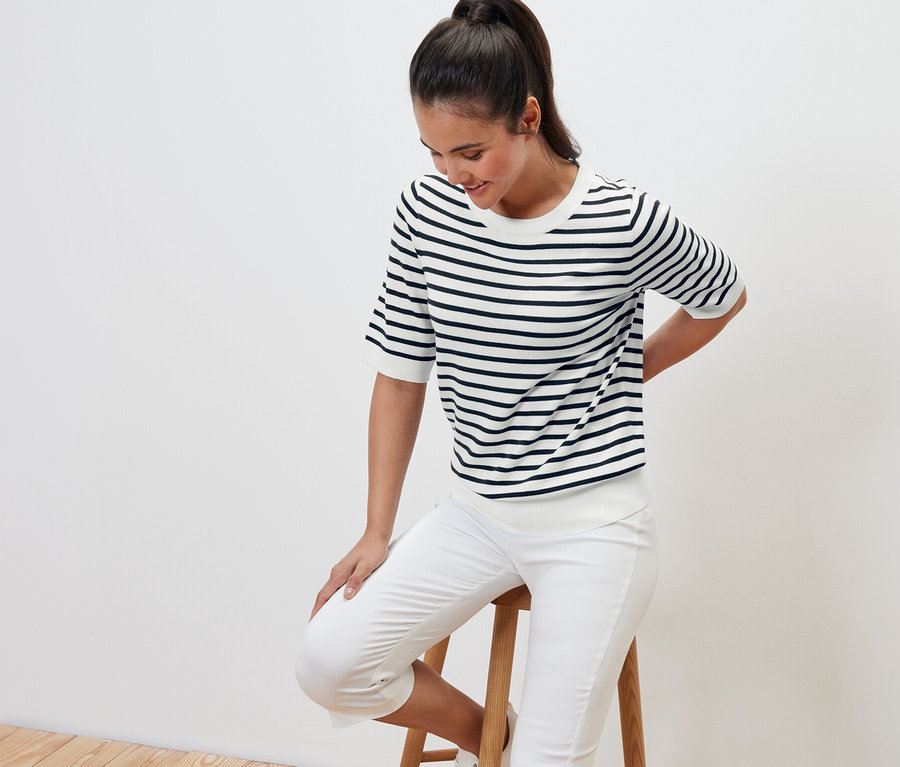Une femme est assise sur un tabouret et porte un pull en tricot fin à rayures bleu marine.
