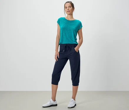 Femme posant en pantalon de survêtement 3/4 bleu foncé et haut bleu-vert.