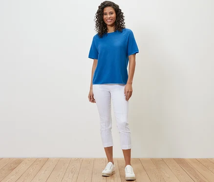 Une femme portant un t-shirt en maille fine bleu cobalt, un pantalon blanc et des baskets blanches.