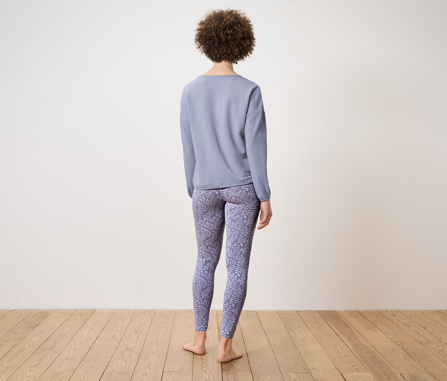 Une femme, vue de dos, porte un haut bleu à manches longues et un legging à motifs.